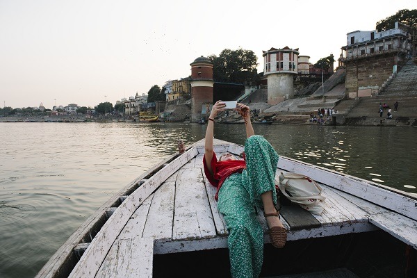 Western Woman Lying On A Boat Taking Selfies In Varanasi