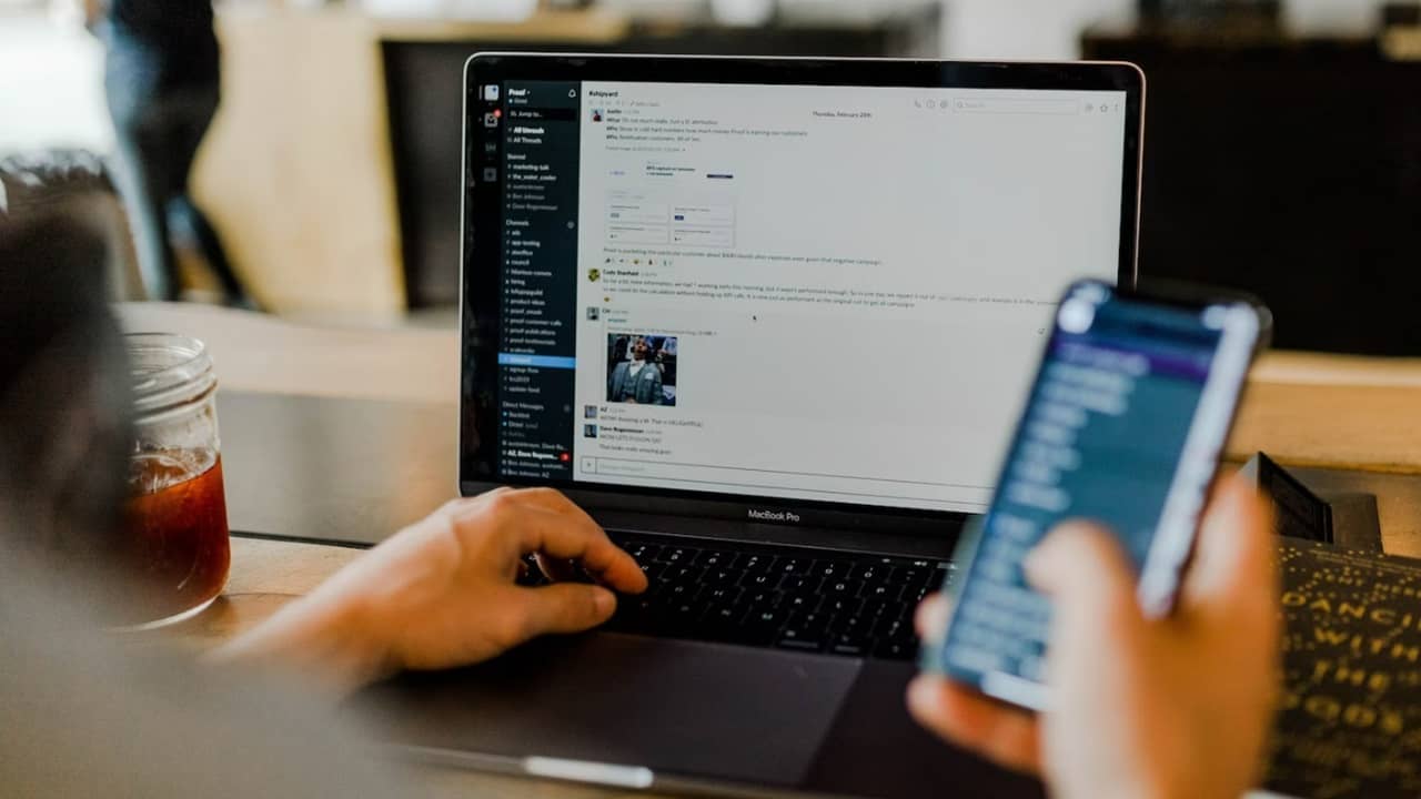 Person using Slack commands on laptop while looking at phone.