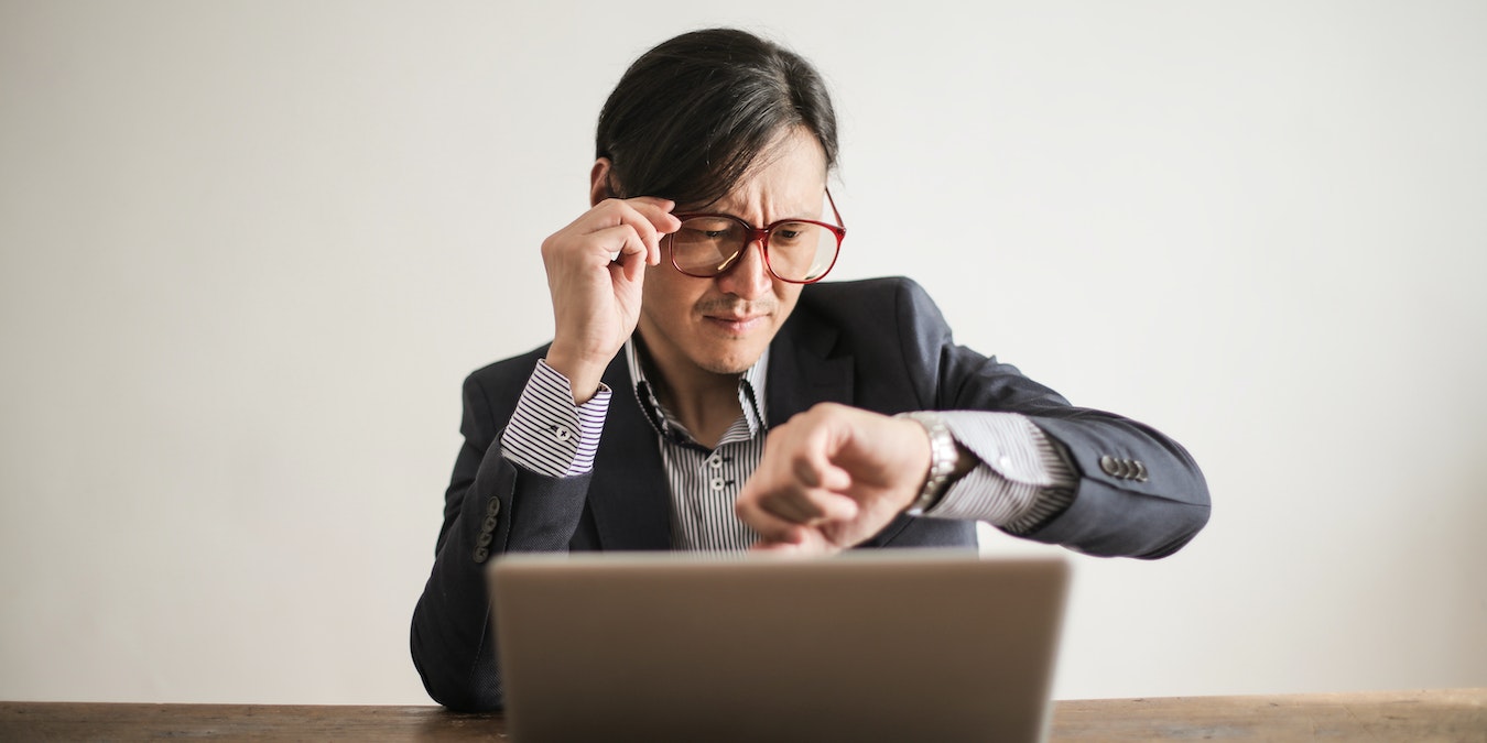 A man who is working on his laptop checks his watch for time