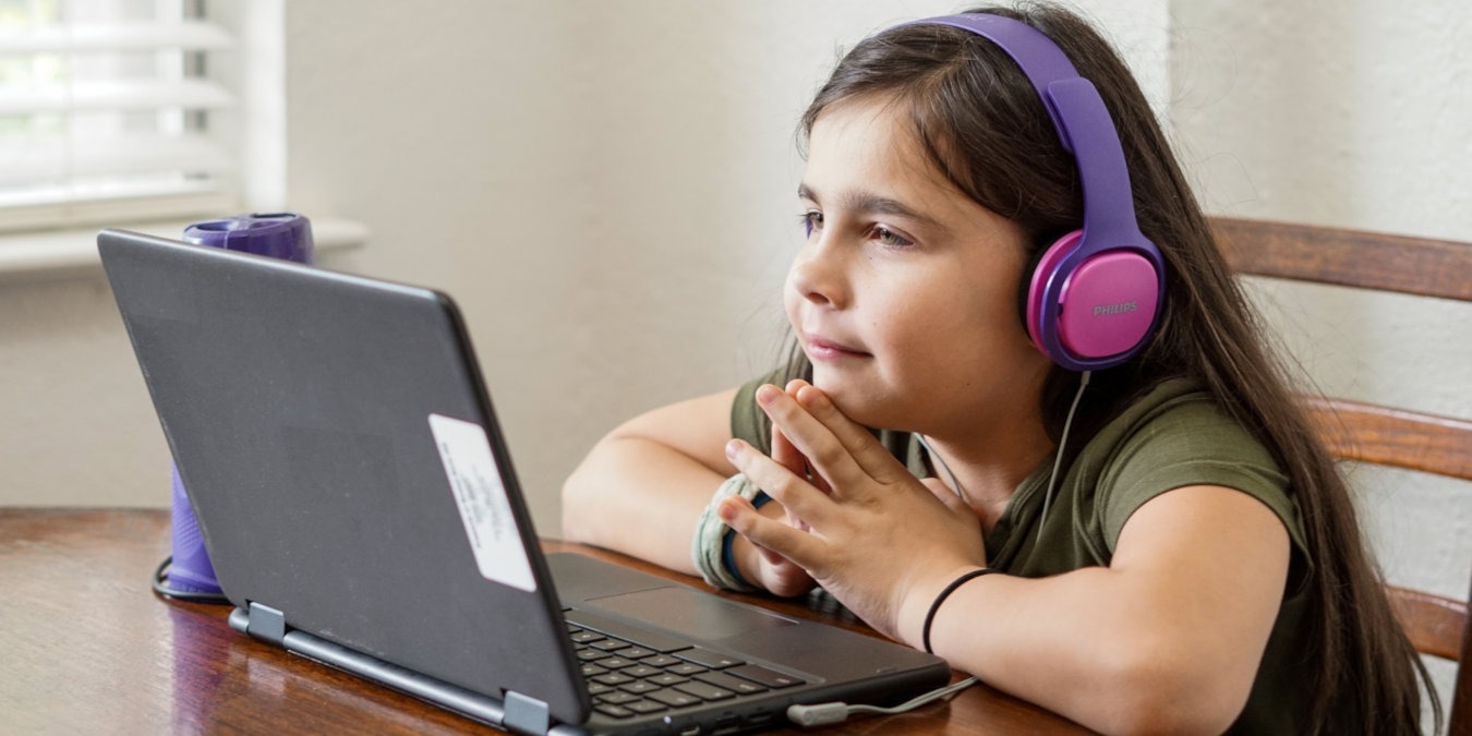 A girl in purple headphones smiling in front of a laptop.