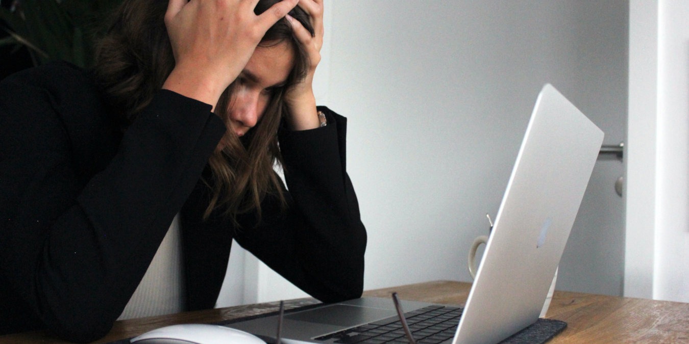 A woman holding her head while staring at a laptop screen.