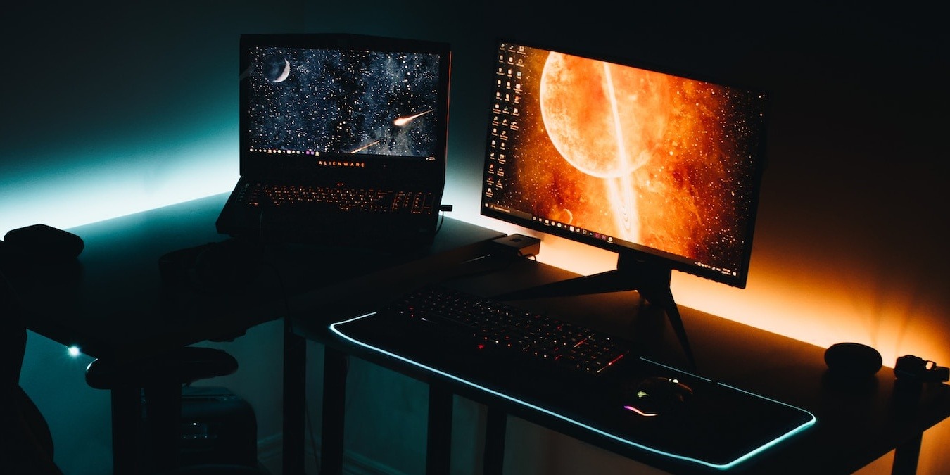 Gaming laptop and gaming monitor side by side on a desk in a dark room