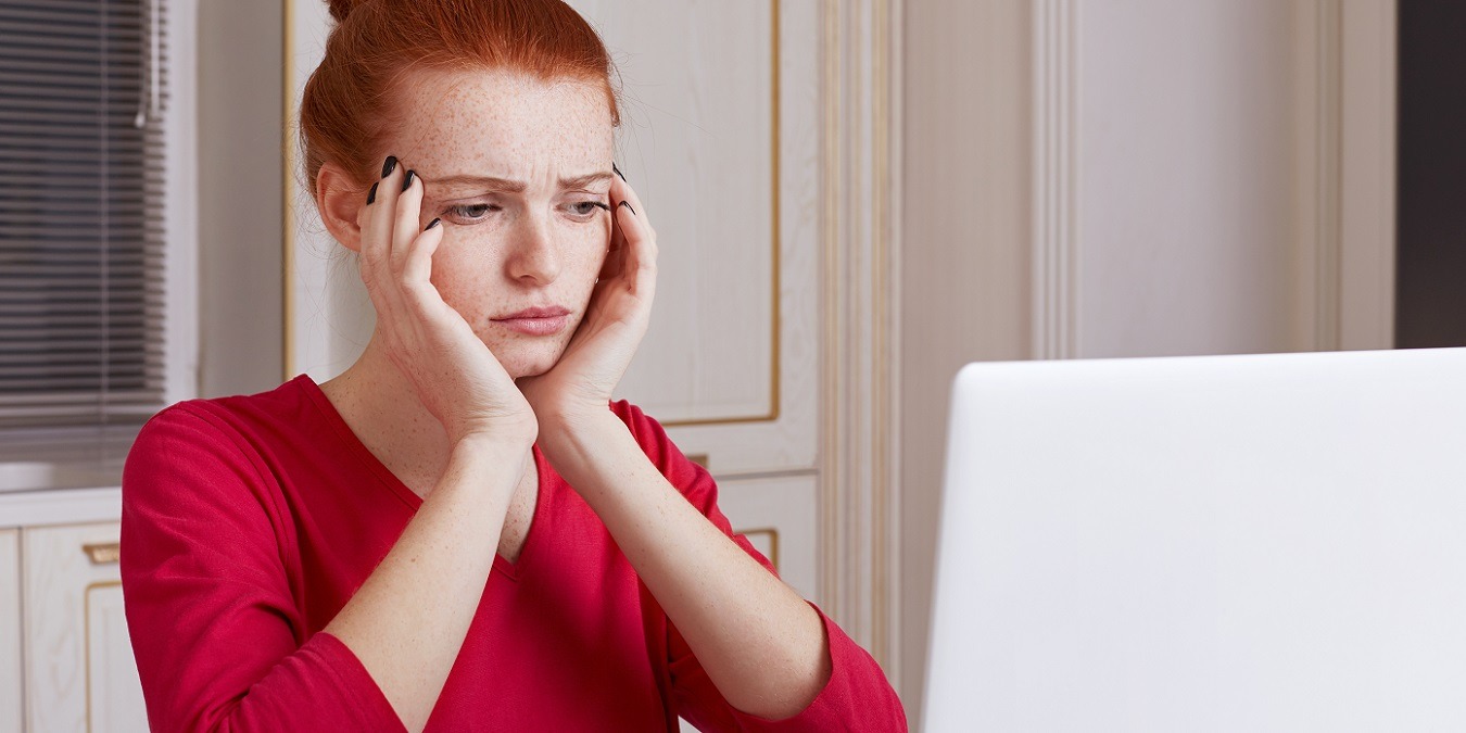 Puzzled Young Female Student Prepares For Exams During Last Day, Reads Material From Laptop Computer, Tries To Remember Something, Sits Over Home Kitchen Interior. Education And Technology Concept