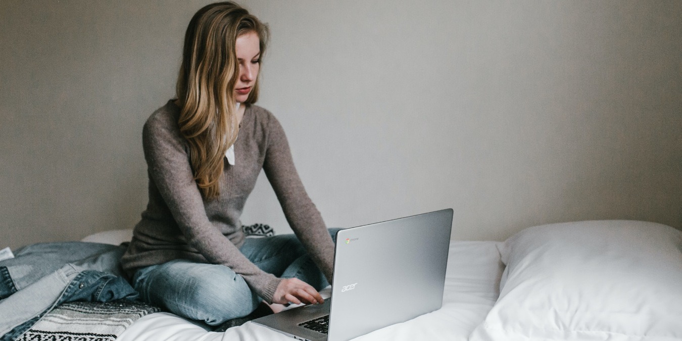 Woman working on Windows laptop while sitting on a bed