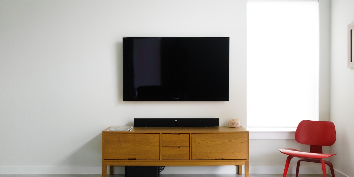 Large screen TV on white wall with a brown TV stand and red chair