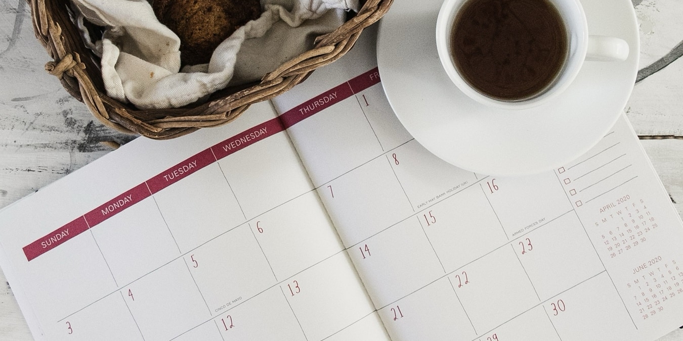 Date planner on a desk with coffee and a snack