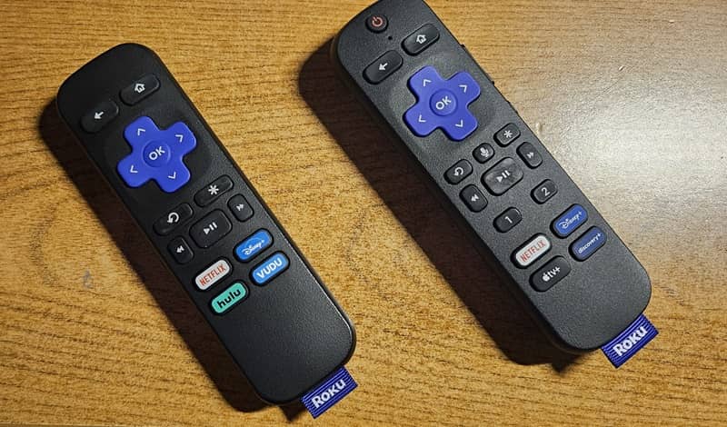 A Roku simple remote and a Roku voice remote sitting side by side on a table.