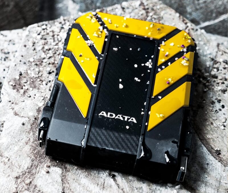 Adata HD710 Pro 2TB Yellow and black external hard drive on a white surface in the outdoors