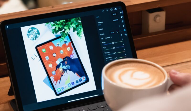 Person holding a coffee cup near a black iPad with a keyboard