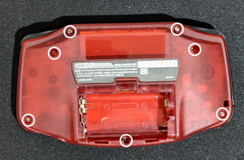 A Game Boy Advance highlighting the different screws that will open the device.