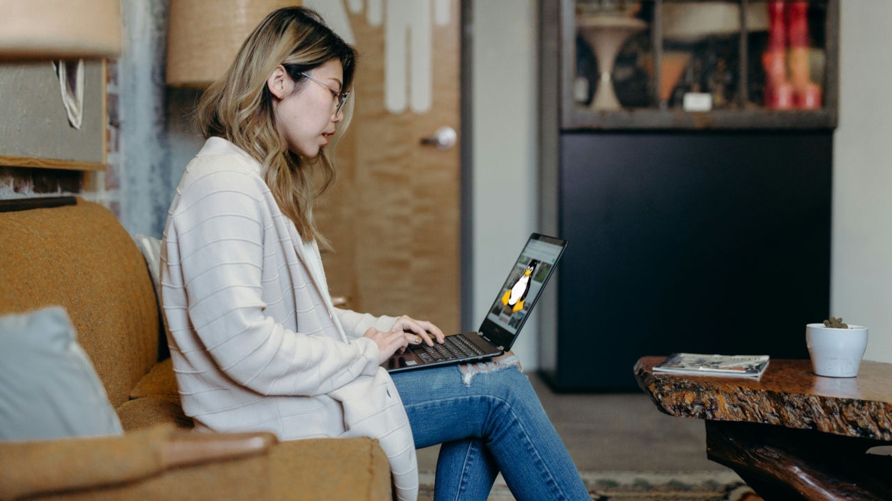 A photograph of a woman sitting in a couch while using her laptop.