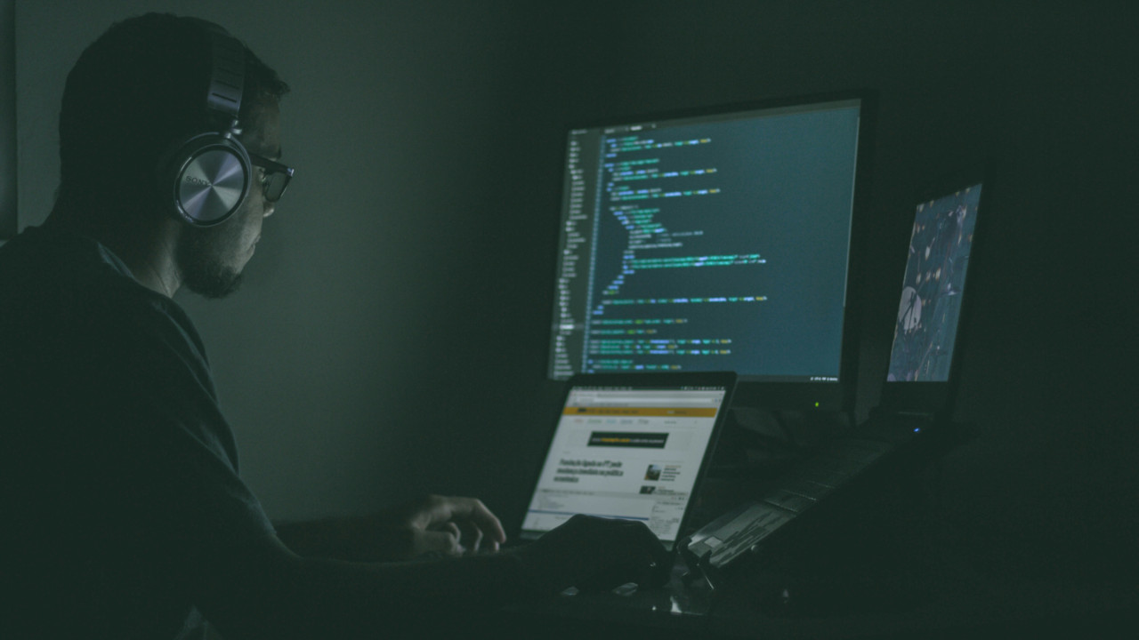 A photograph of a man in a dark room in front of a computer.