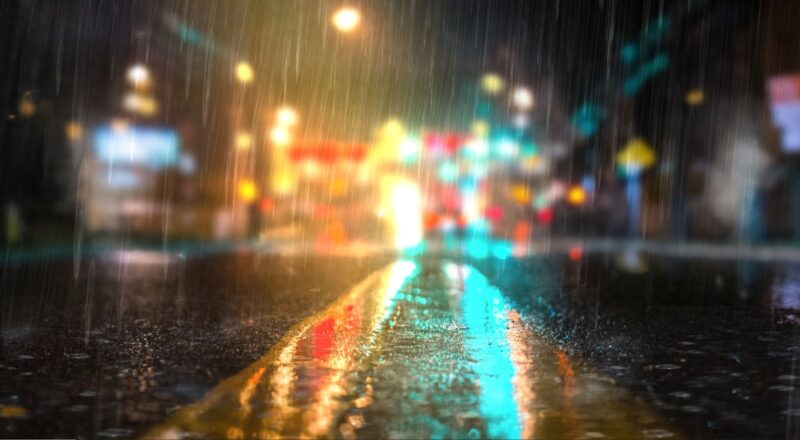 Rain falling on a concrete road with diffused lights in the background