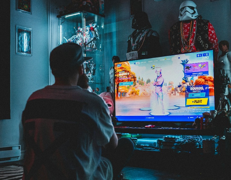 Man sitting and playing a game on a TV with  several figurines in the background