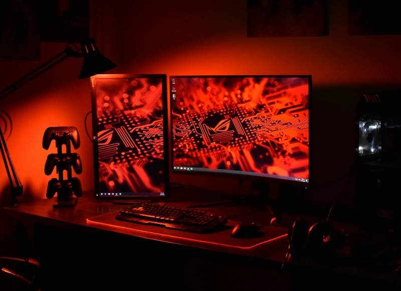 A gaming PC and dual monitors on a desk bathed in red light