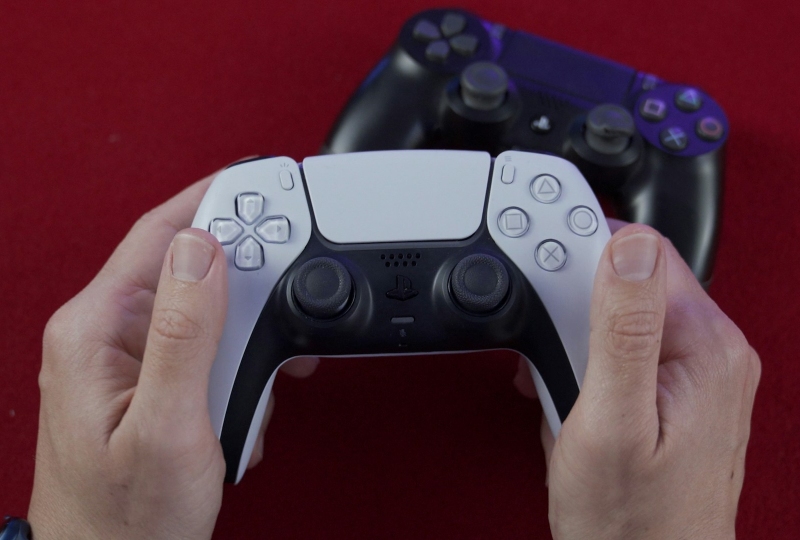 Person holding PlayStation 5 controller with a PlayStation 4 controller in the background