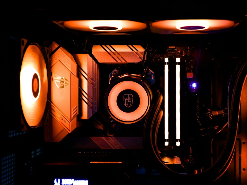 Close-up of a gaming PC showing a CPU cooler, RAM, and fans in orange lighting