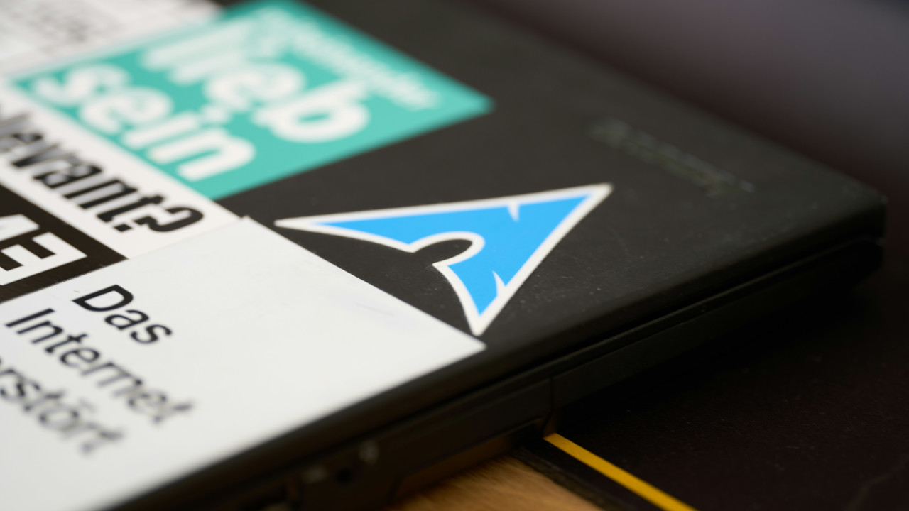 A photograph showing a laptop lid with the Arch Linux sticker on it.