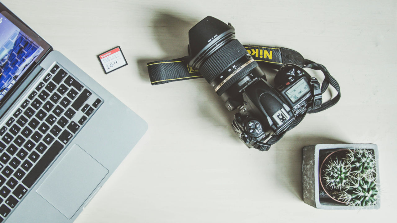 A photograph of a professional camera beside a laptop and an SD card.