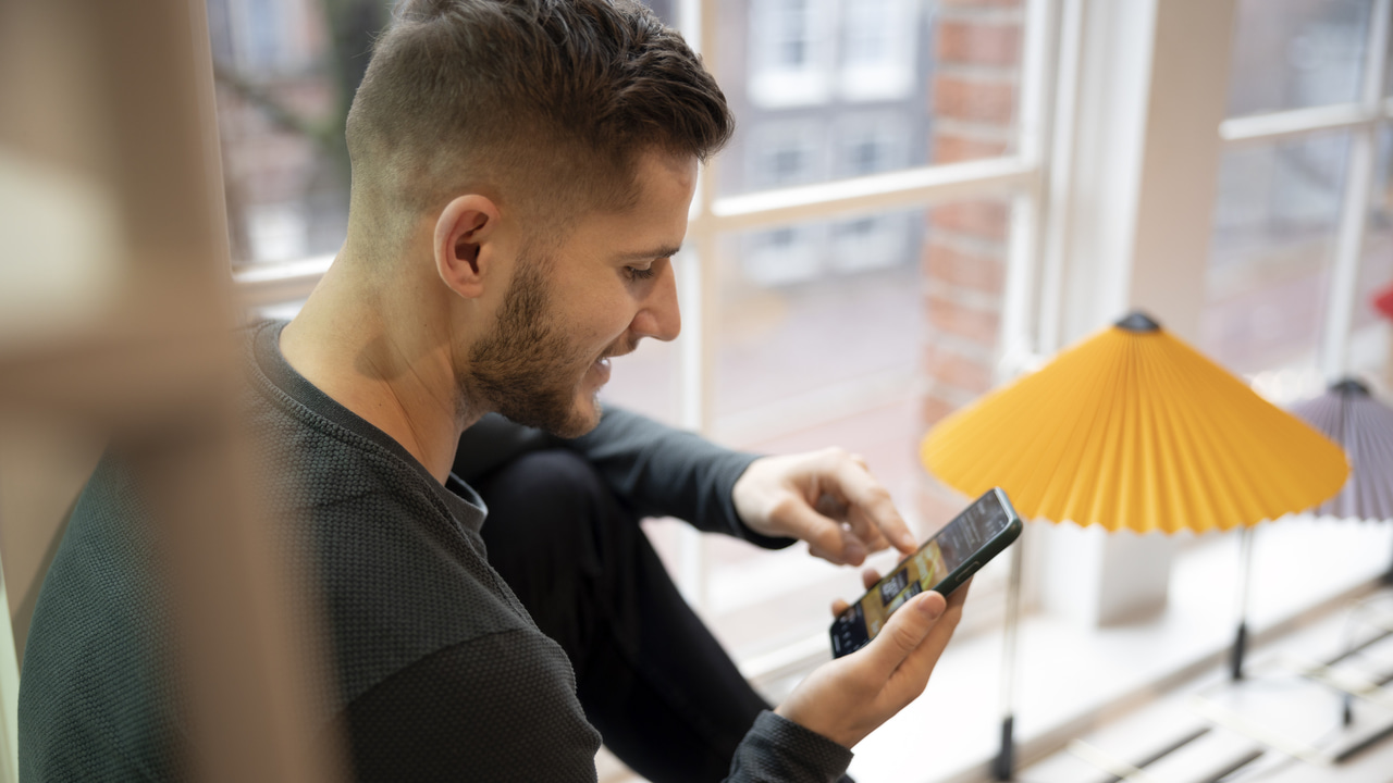 man happily looking at phone in had near window