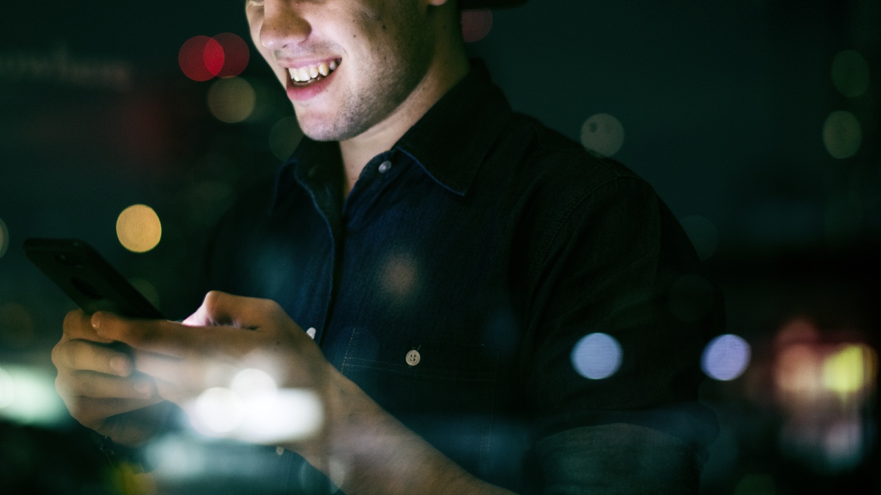 Happy Young Adult Male Using A Smartphone In A Night Cityscape