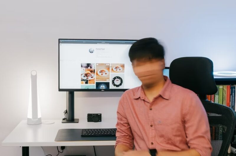 Person with blurred out face in front of a computer desk.