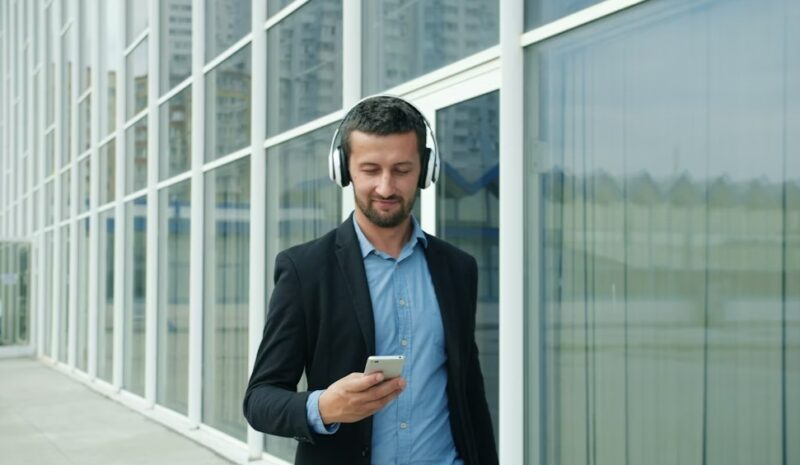 Man in a suit with headphones and phone walking by windows.