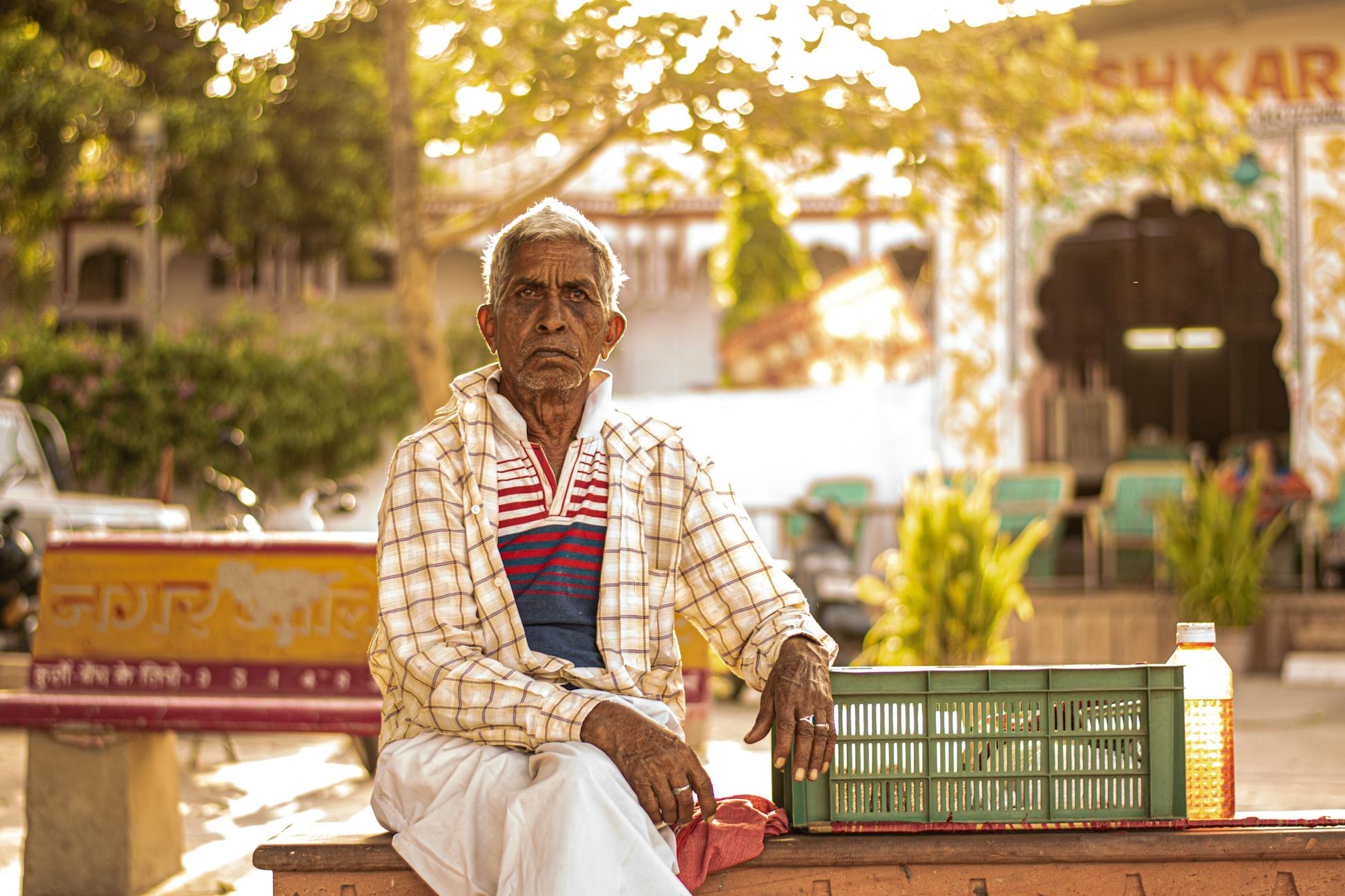 Elderly man in Pushkar, India sitting on a bench in a market setting during daytime.