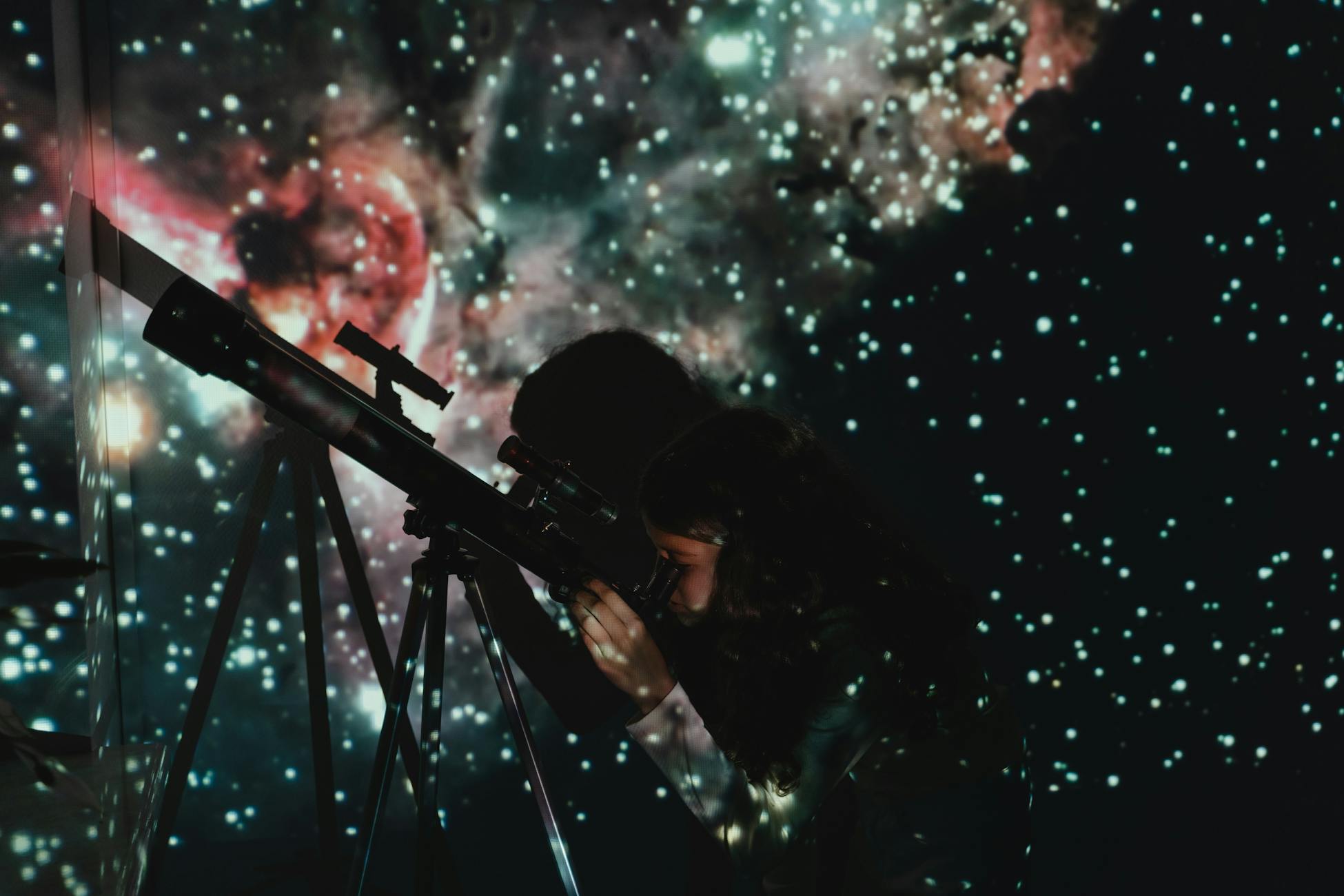 A girl looks through a telescope at a starry projection, blending education with wonder.