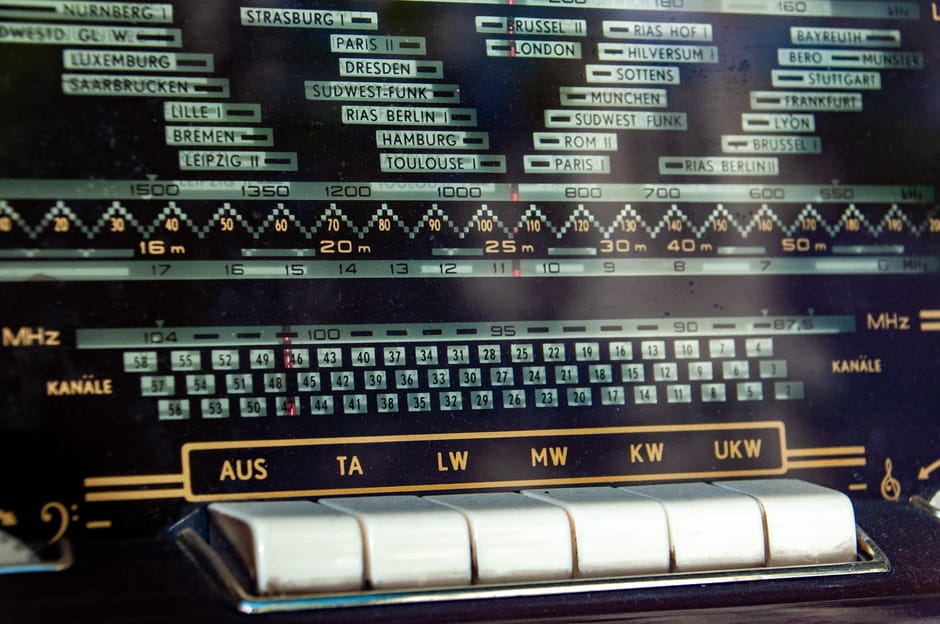 Close-up of a vintage radio dial displaying frequency bands and station names.