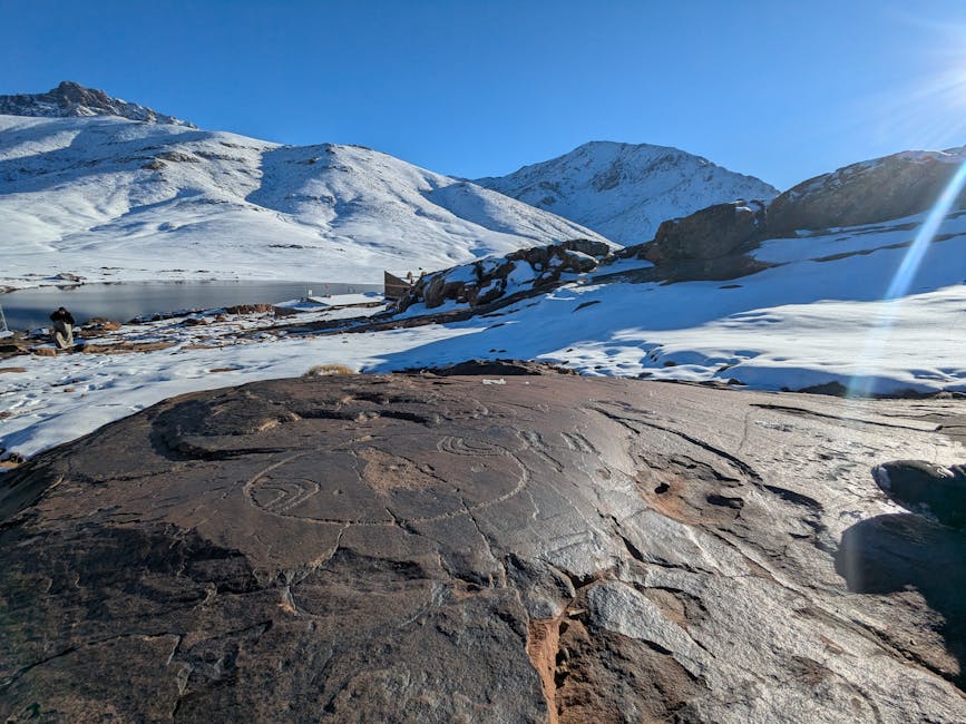 Scenic view of snow-covered mountains with ancient petroglyphs on rocks under a clear blue sky.